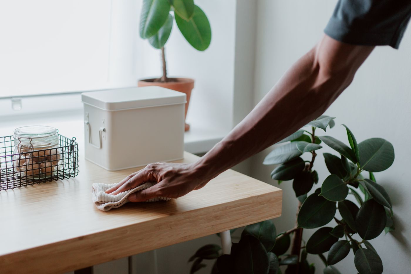 Hand wiping a wooden table with a cleaning cloth.