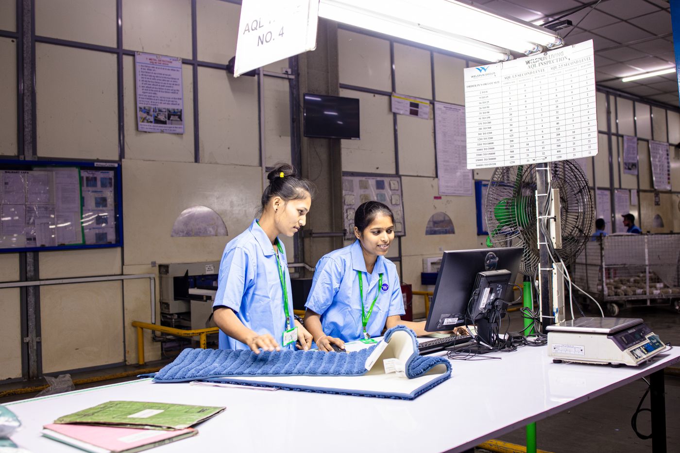 Two female textile workers inspect fabric at a real factory inspection station.