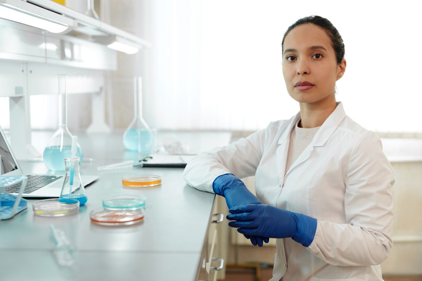 Real scientist at a laboratory bench with glass flasks, petri dishes and gloves.