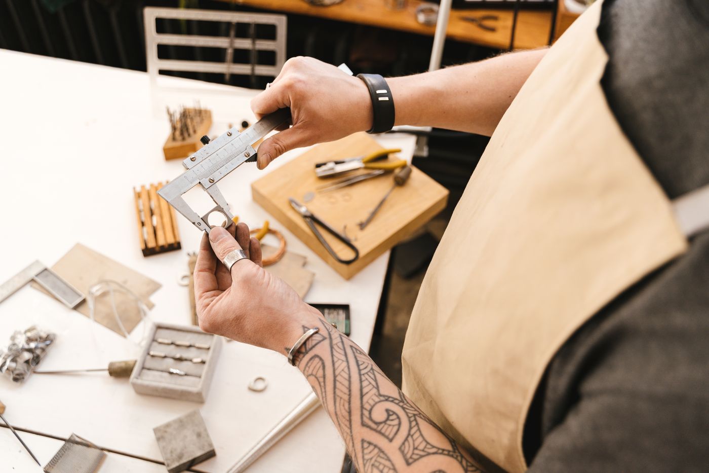 Hands checking an object's dimension with a vernier caliper in a workshop.