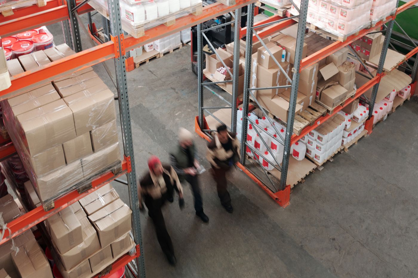 High-angle photograph of workers moving through shelves of cartons in a warehouse.