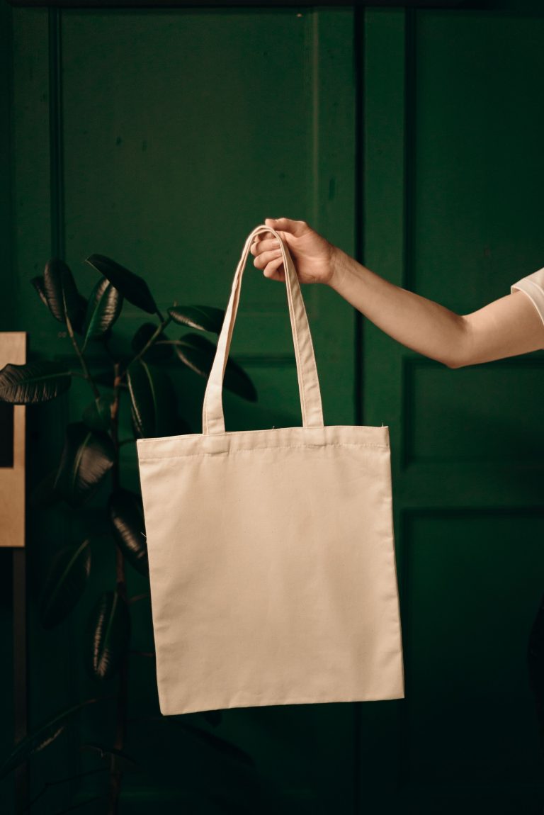 A canvas tote bag held against a dark green background