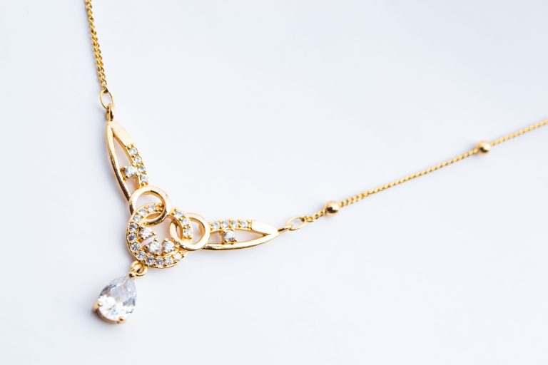 A gold-colored necklace and pendant on a white surface
