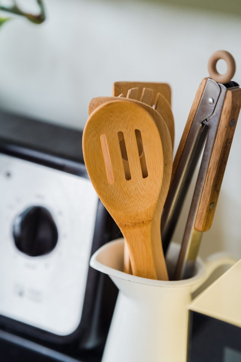 Wooden and metal kitchen utensils in a white container