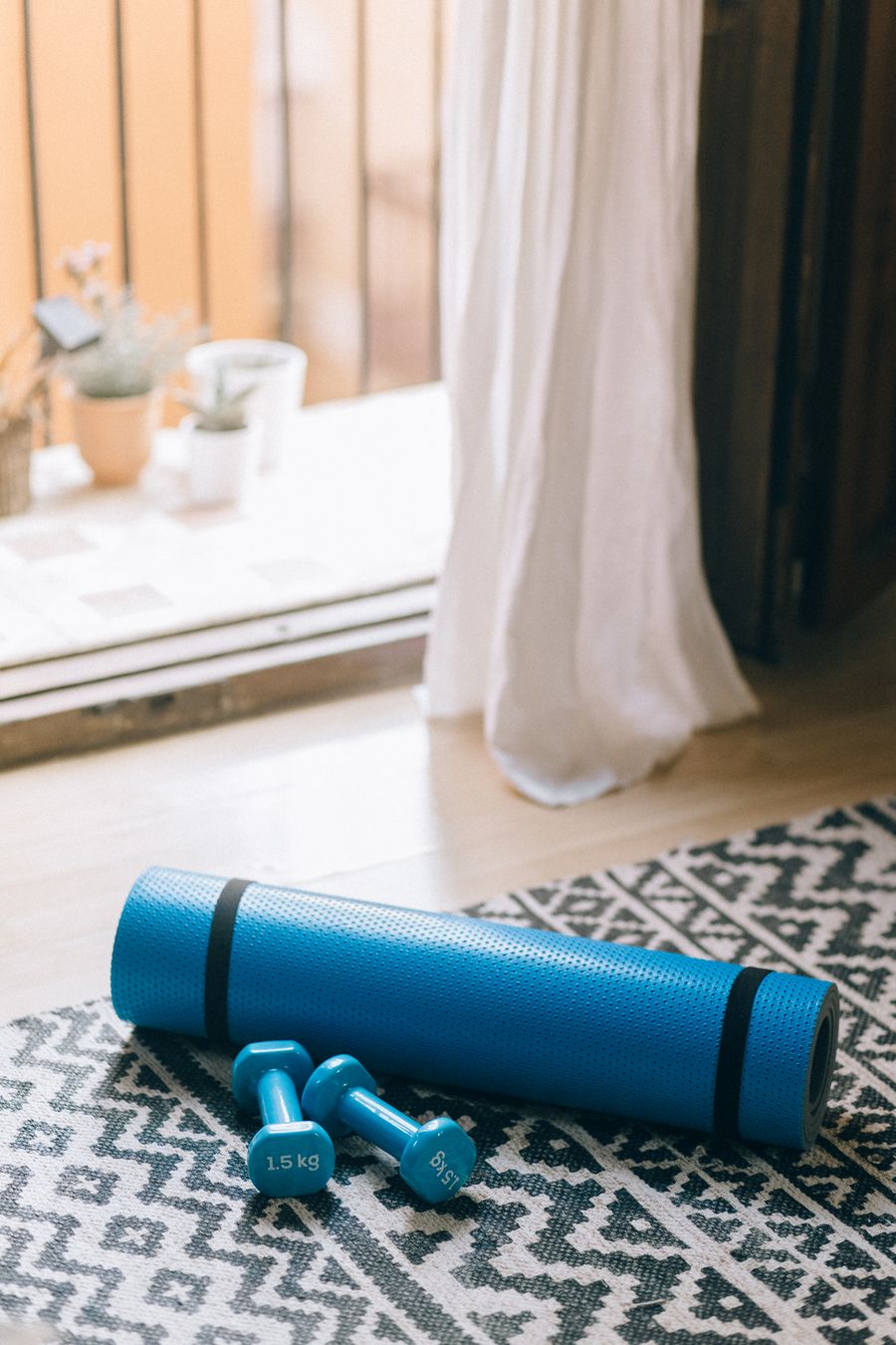 Blue rolled exercise mat and dumbbells beside a window
