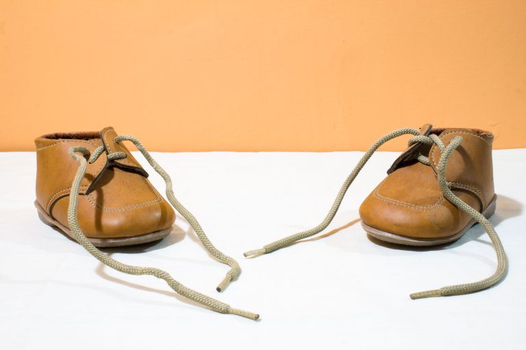 A pair of small tan baby shoes against an orange background